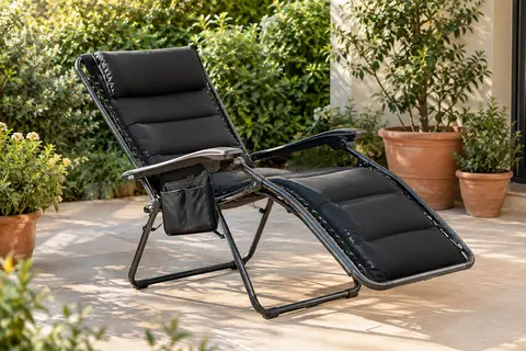 Chaise longue pliable noire à dossier réglable, matelas intégré et poche latérale sur une terrasse végétalisée.