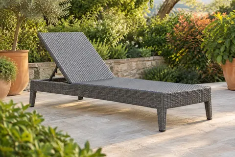 Bain de soleil gris en résine imitation rotin, dossier relevé sur une terrasse végétalisée.