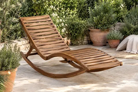 Chaise longue à bascule en acacia brun installée sur une terrasse claire au milieu d’un jardin végétalisé.