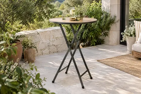 Table haute pliante ronde à plateau aspect bois installée sur une terrasse végétalisée
