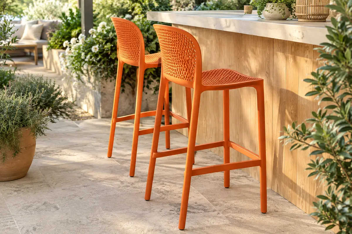Deux tabourets de jardin orange en polypropylène, avec dossier arrondi et repose-pieds, sur une terrasse végétalisée.