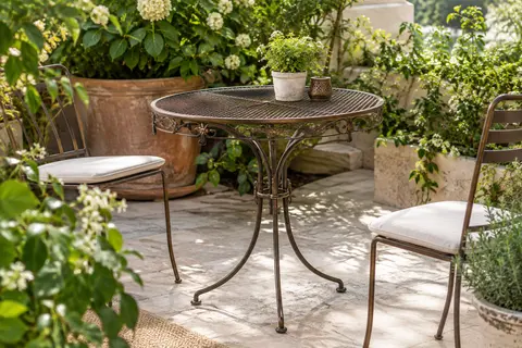 Table bistrot ronde en fer bronze à plateau ajouré, installée sur une terrasse végétalisée