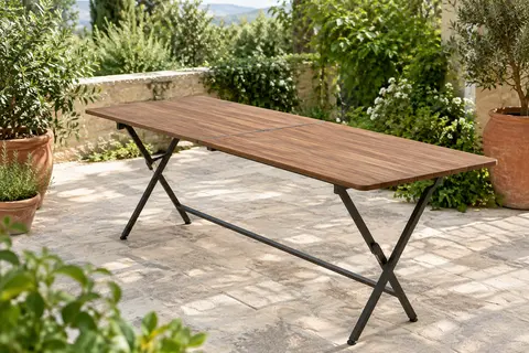 Table de jardin pliante en bois brun, installée sur une terrasse végétalisée lumineuse.