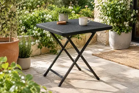 Table de jardin pliante noire à plateau imitation rotin, installée sur une terrasse végétalisée
