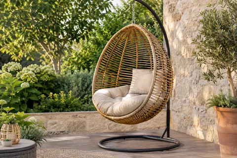 Fauteuil suspendu en polyrattan avec support en acier et coussin beige, installé sur une terrasse végétalisée.