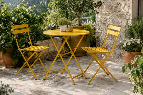 Ensemble bistrot jaune en acier avec table ronde et deux chaises pliantes sur une terrasse végétalisée