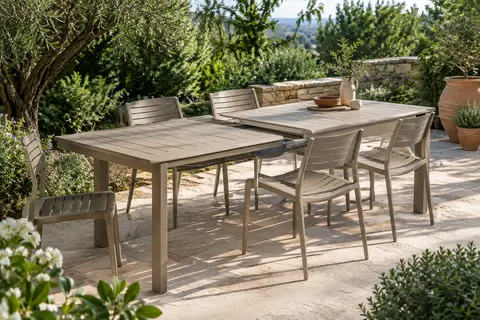 Table de jardin extensible en aluminium argile installée sur une terrasse entourée de végétation.