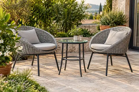 Salon bas gris clair avec deux fauteuils tressés et une table ronde en verre sur une terrasse végétalisée.