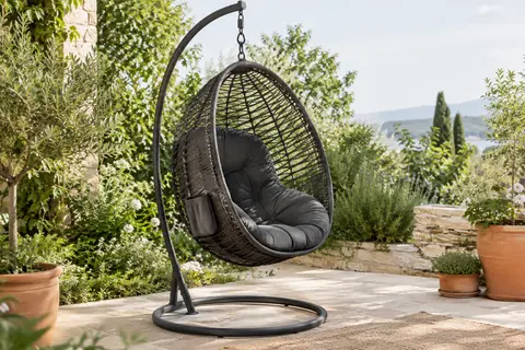 Fauteuil suspendu anthracite avec cadre en acier, coussin et poche latérale dans un jardin végétalisé.