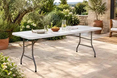 Table pliante blanche Lifetime installée sur une terrasse de pierre claire au milieu d’un jardin verdoyant.