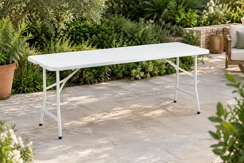 Table pliante blanche ouverte sur une terrasse de jardin, avec plateau en PEHD et piètement en acier.