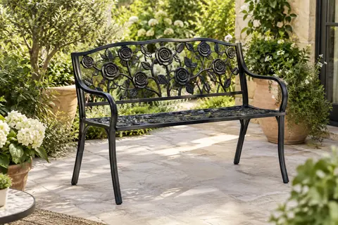 Banc de jardin noir à motifs de roses, avec accoudoirs et pieds inclinés, installé sur une terrasse végétalisée.