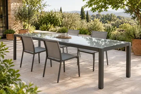 Table de jardin extensible en verre trempé transparent, installée sur une terrasse végétalisée.