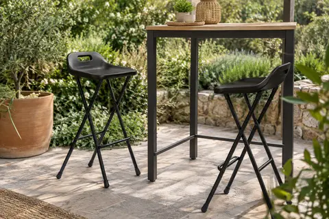 Deux tabourets hauts noirs pliants en acier et résine près d’un mange-debout sur une terrasse végétalisée.