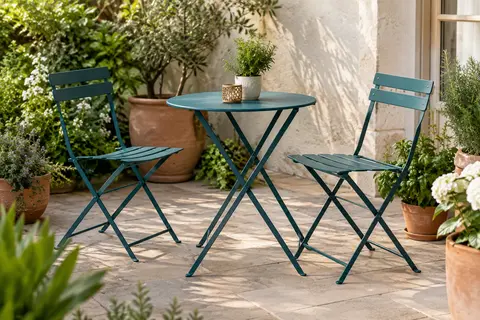 Ensemble bistrot bleu paon avec table ronde et deux chaises pliantes sur une terrasse végétalisée.