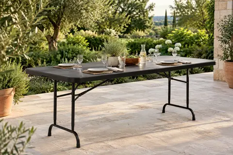 Table pliante rectangulaire noire de 180 cm installée sur une terrasse de jardin végétalisée.