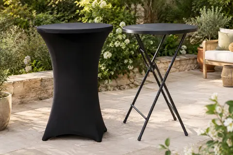 Deux tables hautes pliantes noires, dont une habillée d’une housse, sur une terrasse de jardin végétalisée.