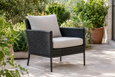 Fauteuil de jardin en polyrotin noir avec accoudoirs et coussins, installé sur une terrasse végétalisée
