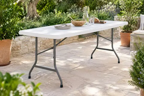 Table de jardin pliante blanche à plateau rectangulaire, installée sur une terrasse végétalisée.