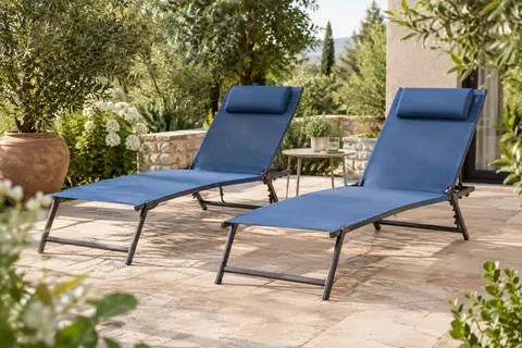 Deux chaises longues pliantes bleues en textilène installées sur une terrasse entourée de végétation.