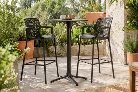 Deux tabourets de bar noirs à dossier ajouré installés autour d’une table haute sur une terrasse végétalisée.